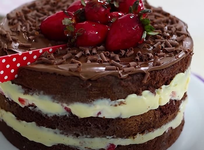 Bolo de chocolate fofinho recheado com creme branco e morangos e coberto por brigadeiro de chocolate